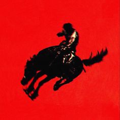 a man riding on the back of a black horse in front of a red background