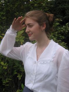 a woman wearing a white blouse and blue skirt holding her hand up to her head