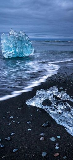 an iceberg floating in the ocean next to a black beach with rocks and pebbles