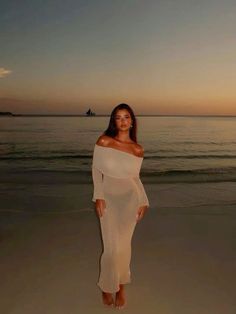 a woman standing on top of a sandy beach next to the ocean at sunset or dawn