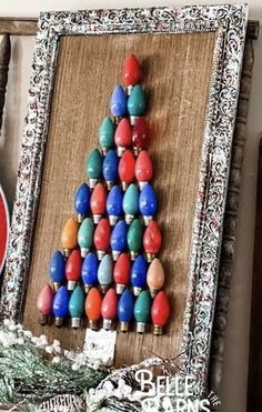 a christmas tree made out of beads is displayed in a frame on a shelf next to other items