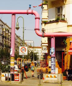 people are walking down the street in front of some buildings with pink pipes on them