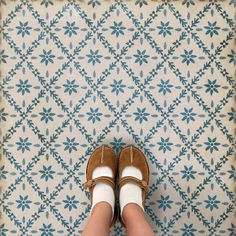 a person wearing brown shoes standing in front of a blue and white patterned wallpaper