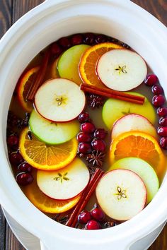 apples, oranges and cranberries are in a white bowl with cinnamon sticks