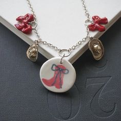 Add a one of a kind piece to your jewelry collection with our handmade polymer clay charm necklace! Each necklace is handmade to order. The necklace features a mix of charms made from high-quality polymer clay coated in resin and silver colored charms. This boot and bow charm necklace contains silver cowgirl hat charms, red clay bows, and a pendant with a red cowgirl boot graphic. Features a lobster clasp closure. Every necklace is handmade from start to finish! Polymer Clay Charms Jewelry For Gifts, Red Polymer Clay Necklace For Gift, Unique Handmade Round Pendant Charm Necklace, Unique Handmade Charm Necklace With Round Pendant, Handmade Red Clay Jewelry, Handmade Polymer Clay Pendant Necklace, Handmade Adjustable Whimsical Charm Necklace, Handmade Red Dangle Charm Necklaces, Handmade Polymer Clay Whimsical Necklaces