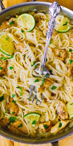 a skillet filled with chicken, noodles and lemons on top of a wooden table