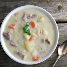 a bowl of soup with carrots, potatoes and meat in it on a wooden table