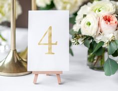 a table with flowers and a card holder on it that has the number four in gold