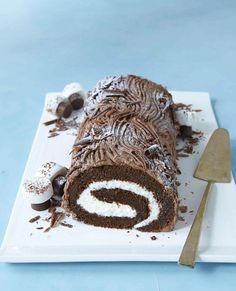 a chocolate roll with white frosting on a plate next to a knife and spoon