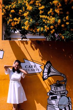 a woman standing in front of a yellow wall with flowers growing out of the window