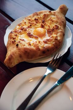 an egg in the shape of a pizza on a plate with fork and knife next to it