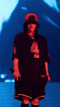 a man with long hair wearing a red hat and black shirt is standing in front of a large screen