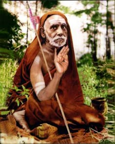 an old man sitting on the ground with a stick in his hand and wearing a brown robe