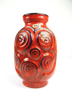 a red vase with swirls on it sitting on a white surface in front of a white background