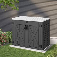 an outdoor storage box in front of a house with grass and flowers on the side