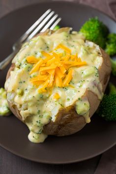 baked potato covered in cheese and broccoli on a plate with a fork next to it