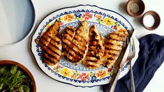 grilled chicken on a plate next to bowls of salad and utensils,