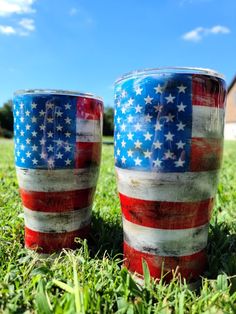 two red, white and blue cups sitting on top of a grass covered field next to each other