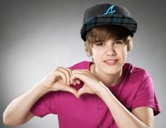 a young man in a pink shirt and cap making a heart shape with his hands