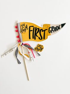 the first grade pennant is on top of a measuring tape and two pencils are next to it