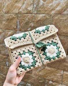 a hand holding up a crocheted purse with flowers on the front and sides