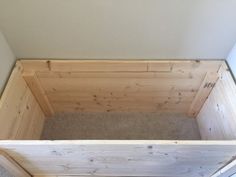 an empty wooden box sitting on top of a carpeted floor next to a wall