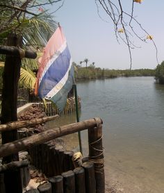 a flag is hanging on the side of a wooden fence next to a body of water