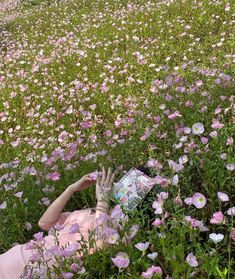 a woman laying in a field of flowers reading a book with her hands on the ground