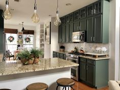 a kitchen with green cabinets and marble counter tops, hanging lights over the stove top