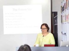 a woman standing at a podium in front of a whiteboard with a presentation on it