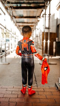 a young boy in black and orange suit standing on brick walkway