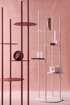 three shelving units with shelves and vases on them in front of a pink wall