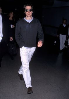 a man walking through an airport carrying a black bag and wearing white pants with his feet in the air