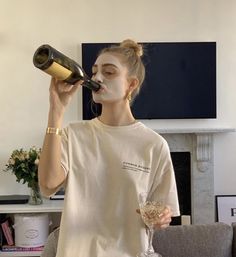 a woman drinking from a wine glass while standing in front of a fireplace