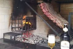 a bottle of beer sitting next to a fire in a brick oven filled with meat