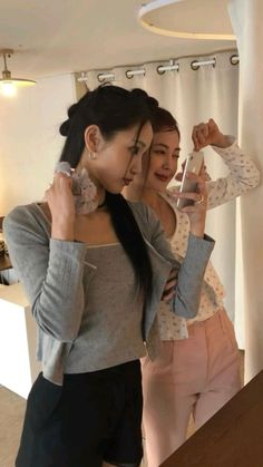 two women standing next to each other in front of a mirror