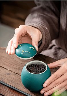 a person is holding a teapot with a cat face on it and some black tea