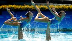 three women in blue swimsuits are jumping into the water with their hands up