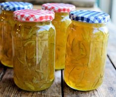 four jars filled with pickles sitting on top of a wooden table