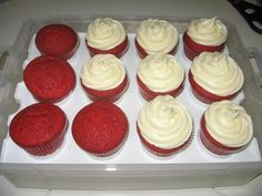 twelve red velvet cupcakes with white frosting in a plastic container on a table