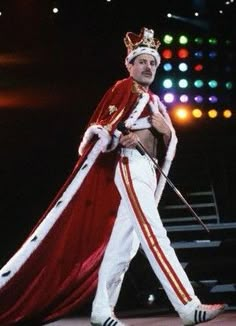 a man dressed in white and red with a crown on his head walking across a stage