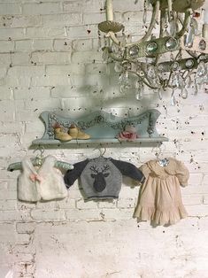 two baby sweaters hanging on a brick wall with a chandelier in the background