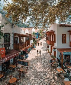 people are walking down an alleyway between two buildings with tables and chairs on it