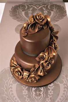 a three tiered chocolate cake with gold flowers on it's top and sides