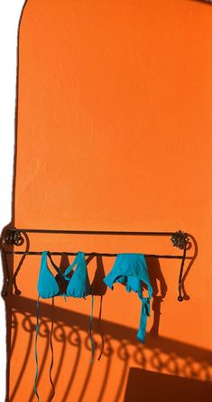 an orange wall with three blue cloths hanging from it's hooks and shadows