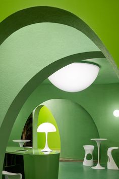 a room with green walls and white chairs in it, as well as round lights on the ceiling