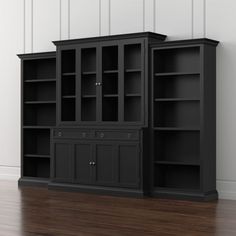 an empty bookcase and cabinet in the corner of a room with hardwood floors, white walls and wood flooring