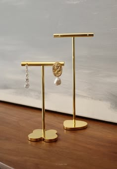 two gold earring stands on top of a wooden table