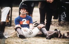 a baseball player sitting on the ground with his helmet and gloves over his face while others stand behind him