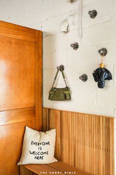 a wooden bench sitting next to a wall with hooks and a purse on it's back